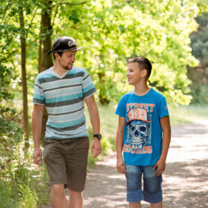 Jugendliche begleiten - ein Teenager und erwachsener Mitarbeiter unterhalten sich lachend während sie auf einem Weg im Grünen spazieren.