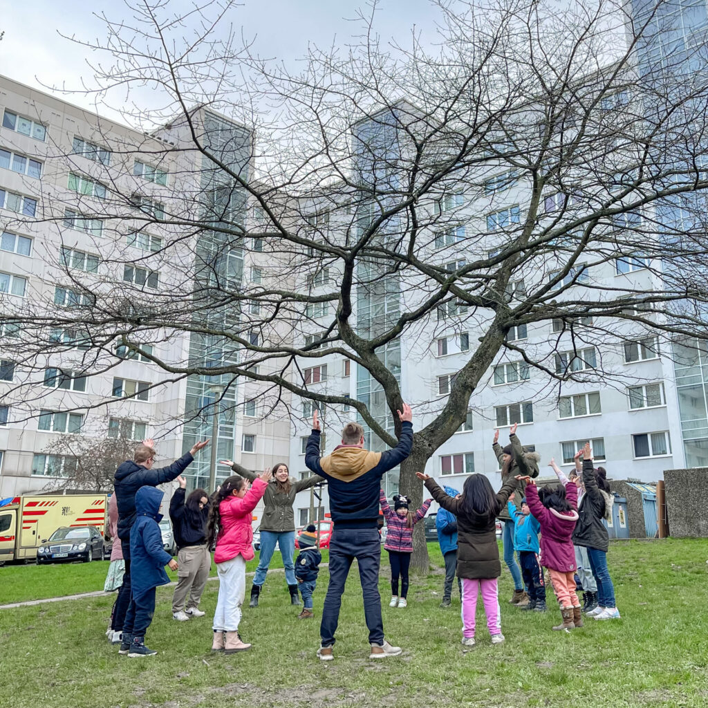 Kindergruppe im Winter beim Kinderprogramm mit Spielen auf der Wiese vor Plattenbauten